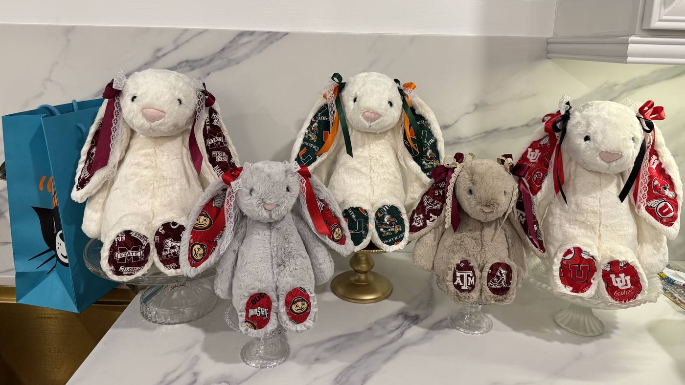 Five handmade bunnies sitting in a row on a marble counter, each with patterned inner ears, matching paw pads and ribbon bows in different color combinations